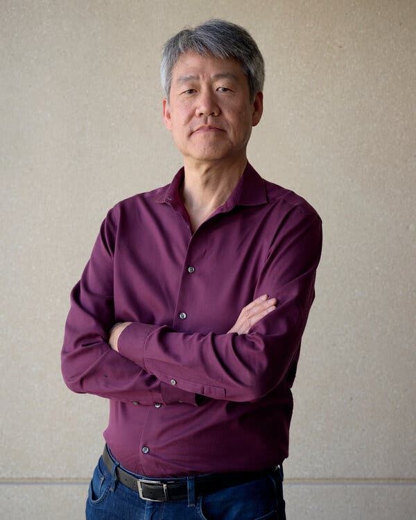 A man, wearing a purple shirt and jeans, poses for a photograph.